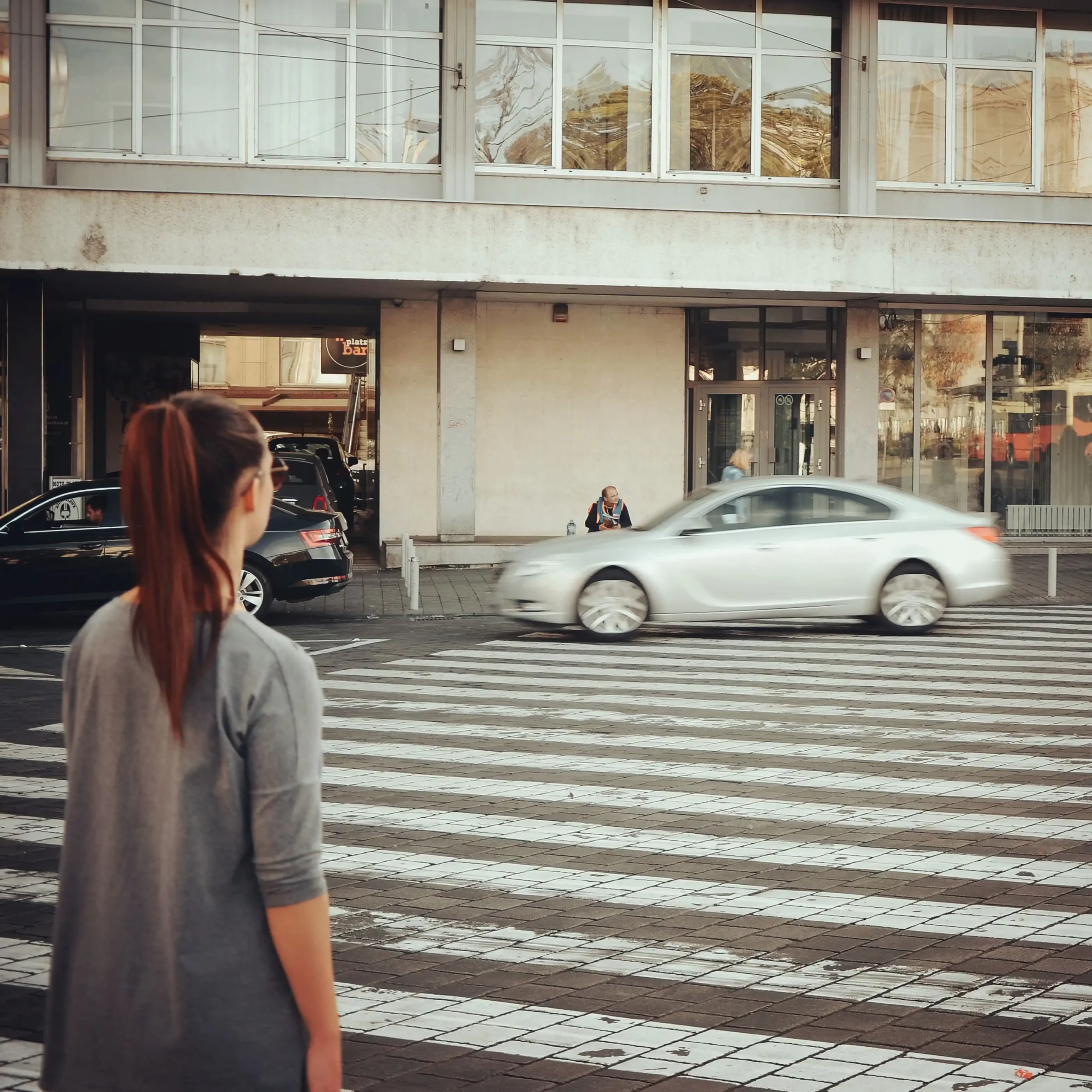 pexels photo 14266475 14266475 scaled A woman stands at a city pedestrian crossing as cars pass by.